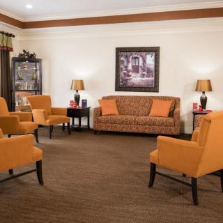 A cozy living room with armchairs and a sofa arranged around a central space, accented by warm lighting and artwork on the wall.
