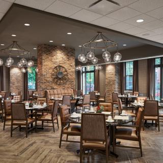 A cozy restaurant interior with neatly arranged tables and chairs, featuring a brick wall and modern lighting fixtures.