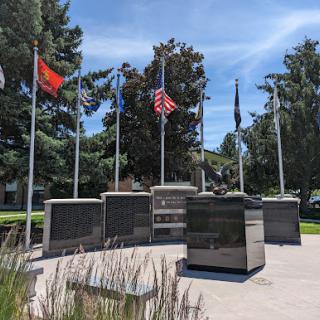 A memorial honoring veterans, surrounded by various flags, set against a clear blue sky.