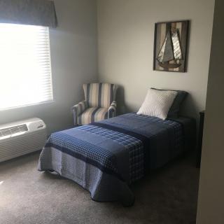 A simple bedroom with a single bed, striped chair, and wall art.
