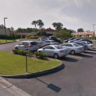 A view of a parking lot filled with various cars surrounded by green grass.