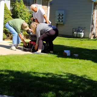 A group of people collaborating on a lawn mower repair in a sunny yard.