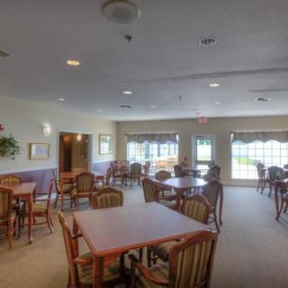 An empty dining room with several tables and chairs, well-lit by natural light through the windows.