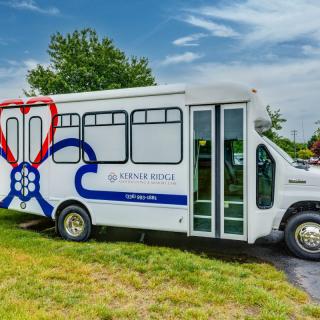 A white bus with colorful designs parked on a grassy area under a cloudy sky.