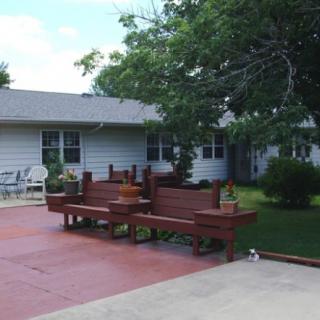 A cozy backyard with a patio, wooden benches, and lush greenery.
