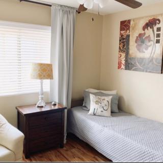 A cozy bedroom with a single bed, a nightstand with a lamp, and decorative artwork on the wall.