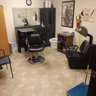 An interior view of a small barbershop with a styling chair, mirror, and salon equipment.