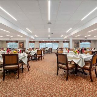 A spacious dining room with neatly arranged tables and chairs, featuring warm lighting and a carpeted floor.