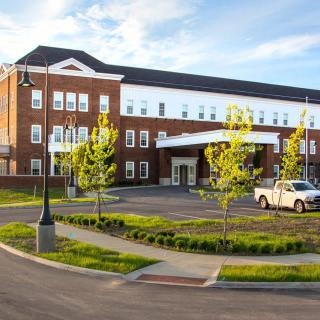 A modern hospital building with a neatly landscaped exterior and a parking area in the foreground.