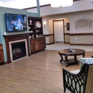 A cozy living room with a television above the fireplace, featuring comfortable seating and wooden flooring.