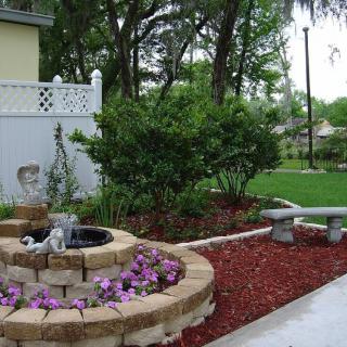 A beautifully landscaped garden with a small water fountain, vibrant flowers, and a stone bench.