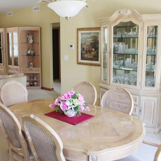 A cozy dining room featuring an elegant table with a floral centerpiece, surrounded by chairs and a china cabinet displaying fine glassware.