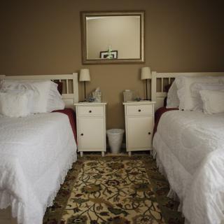 A cozy bedroom featuring two twin beds with white bedding, flanked by nightstands and lamps, with a decorative rug on the floor.