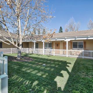 A sunny day view of a house with a porch, yard, and tree.