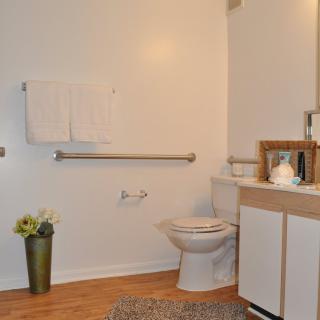 A simple and clean bathroom with a toilet, vanity, and grab bars for accessibility.