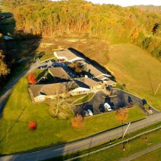 Aerial view of a building surrounded by autumn trees and a road with parked cars.