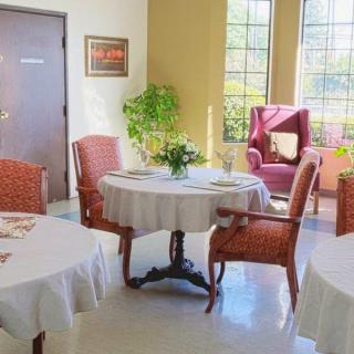 A cozy dining area with tables and chairs, warmly lit by sunlight streaming through the windows.