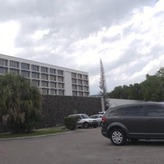 A view of a hotel building with vehicles parked in the foreground under a cloudy sky.