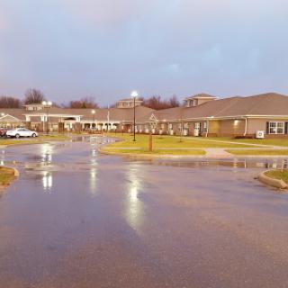 A view of a medical facility during a rainy evening, reflecting lights on the wet pavement.