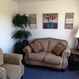 A cozy living room with a sofa, armchair, indoor plant, and wall art.