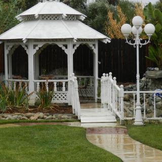 A white gazebo in a landscaped garden with a pathway and a lamp post.