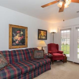 A cozy living room featuring a plaid sofa, red armchair, ceiling fan, and decorative artwork.