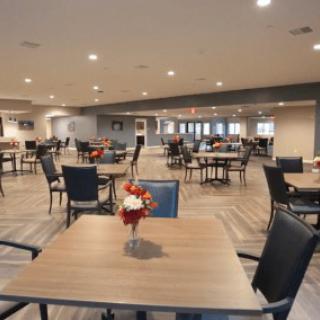 An empty dining room with neatly arranged tables and chairs, featuring a floral centerpiece on each table.