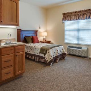 A cozy bedroom with a single bed, window, and wooden cabinetry.