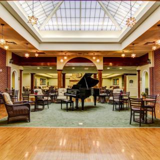 A spacious lobby with a grand piano, surrounded by seating areas and illuminated by a skylight.