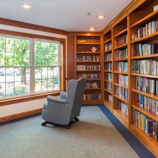 A peaceful reading nook featuring a comfortable armchair and well-stocked bookshelves, bathed in natural light from a large window.
