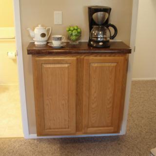 A small kitchen setup with a cabinet featuring a coffee maker, teapot, and cups on top.