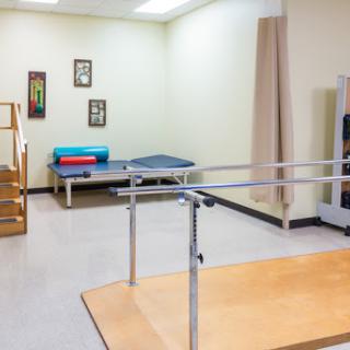 A well-equipped physical therapy room featuring parallel bars and a treatment table.