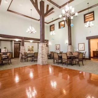 A spacious dining hall with chandeliers, wooden floors, and elegantly arranged tables and chairs.