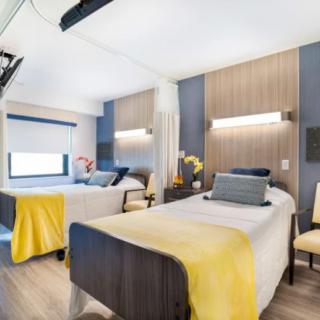 A modern hospital room with twin beds and yellow accents.