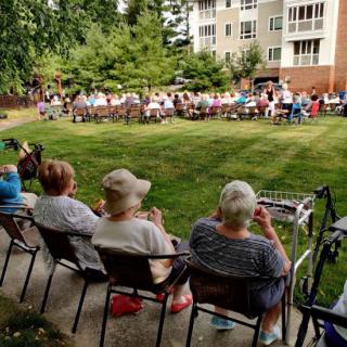 A group of seniors sitting outdoors, attending a community event in front of a residential building.
