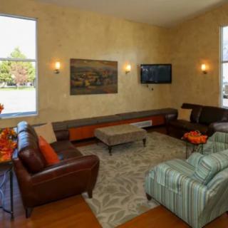 A cozy living room with sofas, armchairs, and a coffee table, adorned with wall art and a television.