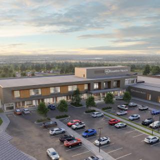 Aerial view of a modern building with a spacious parking lot and scenic landscape in the background.