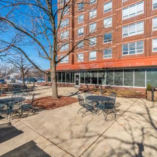 An outdoor patio area with tables and chairs near a tall brick building on a sunny day.