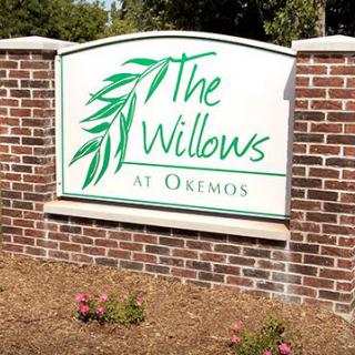 A sign for The Willows at Okemos set in a brick structure with surrounding landscaping.
