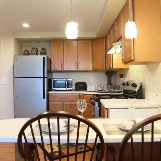 A modern kitchen with wooden cabinets, stainless steel appliances, and a countertop with chairs.