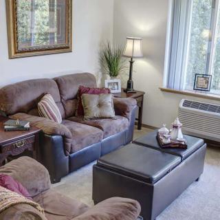 A cozy living room with a sofa, armchair, coffee table, and a lamp by the window.