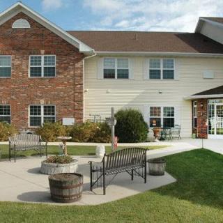 A two-story residential building with a patio area, featuring benches and landscaping.