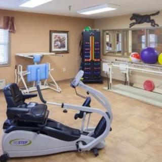 A fitness room equipped with various exercise machines and rehabilitation tools, including a stationary bike and therapy balls.