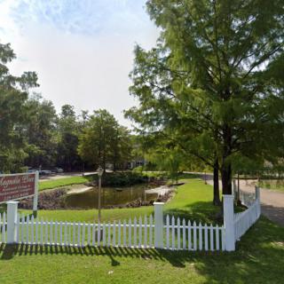 A scenic park with a white picket fence, trees, and a small pond.
