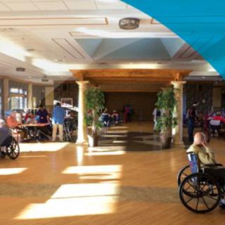 A spacious nursing home interior with residents in wheelchairs.