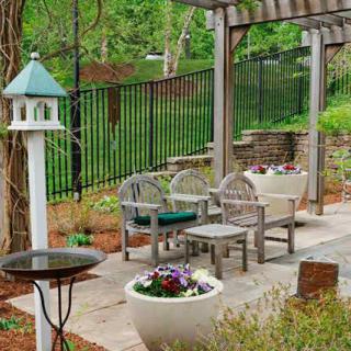 A serene garden setting with outdoor seating, a birdhouse, and vibrant plants under a pergola.