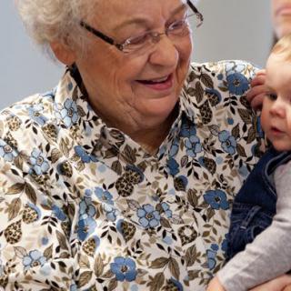 An elderly woman lovingly holds and smiles at a baby, showcasing a warm family bond.
