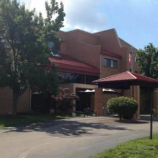 A building with a red roof surrounded by trees and bushes, under a clear sky.