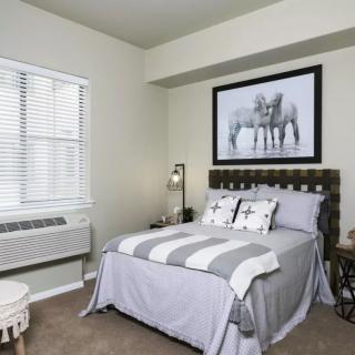 A cozy bedroom featuring a neatly made bed with striped bedding, a framed artwork above the headboard, and a window with blinds.