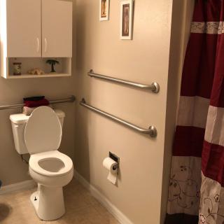 A bathroom featuring a toilet with grab bars, a wall cabinet, and a red shower curtain.